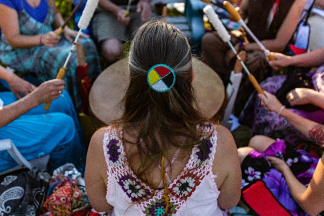 Sacred drums during spiritual singing. A high angle view of a woman wearing native headband and colourful clothes during a singing circle of people around a sacred mother drum outdoors
