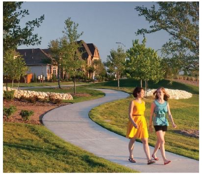 Two people walking along a tree-lined paved pathway