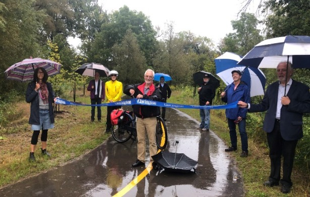 Councillor Hooper and Councillor Zwart hold the ribbon across the trail as Mayor Foster cuts it in the middle at the opening of the Bowmanville Valley Trail extension opening