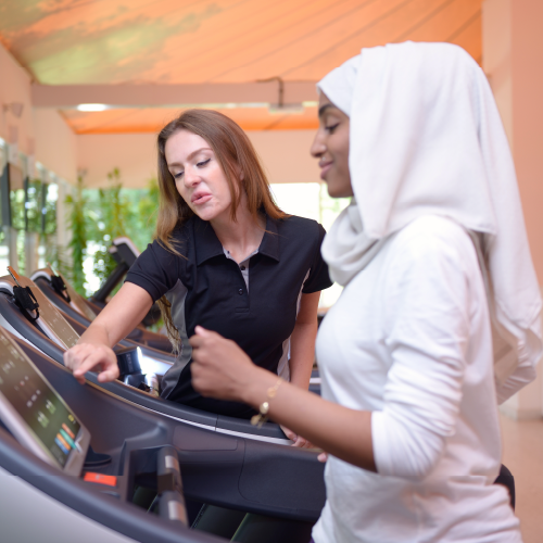 Woman with a head scarf on the treadmill with a personal trainer assisting.