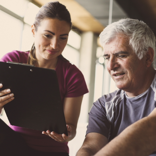 Personal trainer holding a clipboard talking with a fitness client.