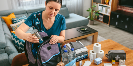 Woman putting cans of food to prepare emergency backpack in living room