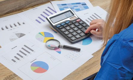 Woman using a calculator with charts and graphs in front of her.