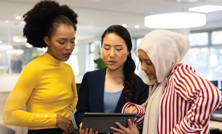 Diverse businesswomen with tablet working and talking in office