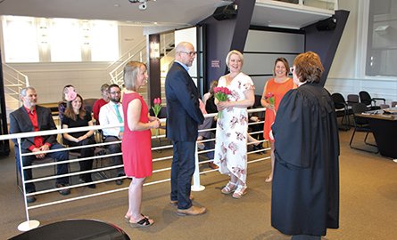 A wedding ceremony taking place in Council Chambers with bride, groom, officiant, witnesses and guests 