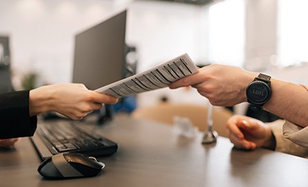 Close-up hands of unrecognizable manager and client exchanging document sitting at desk in office. 