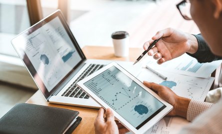 Business meeting with a tablet and laptop with graphs and charts on the screen