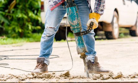 Worker uses a jack hammer on concrete making lots of noise.