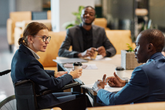 Side view portrait of successful businesswoman using wheelchair at meeting and talking to group of colleagues in modern office space