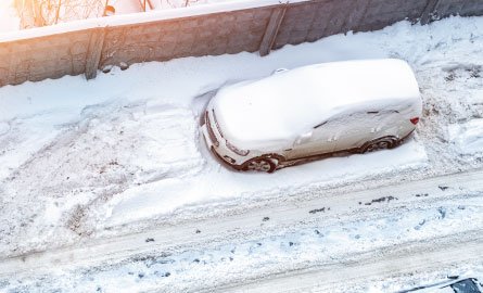 A car parked on the street snowed in by the snow plow.