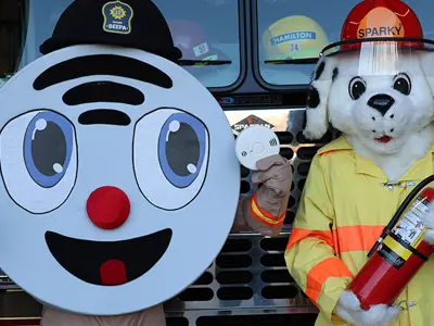Beepa the smoke alarm mascot and Sparky the fire dog mascot in front of a fire truck.