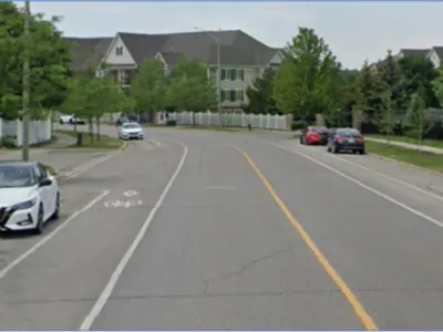 A straight two-lane road in a rural area with white and yellow lines to guide traffic.
