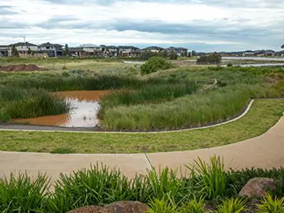 Stormwater management pond with a walking path around it and homes in the distance.