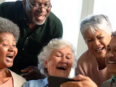 Five happy diverse senior friends sitting on sofa and looking at smartphone.
