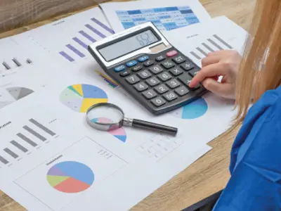 Woman using a calculator with charts and graphs in front of her.