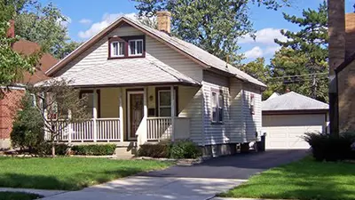 The front yard of a small home showing the yard, driveway, sidewalk and boulevard.