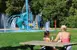 Mom and daughter eating ice cream on a picnic table with a splash pad in the background.