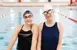Two young women smiling in the the pool with goggles and swimcaps.