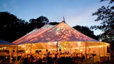 Special event tent lit up from the inside with dark blue night time sky and trees
